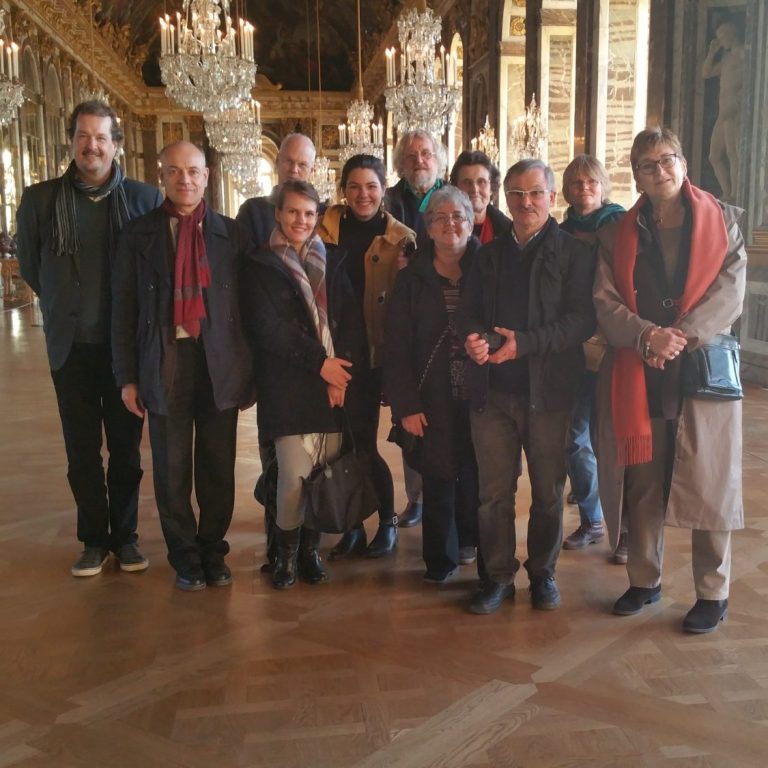 A group of thirteen people posing together in an ornate, historic building.