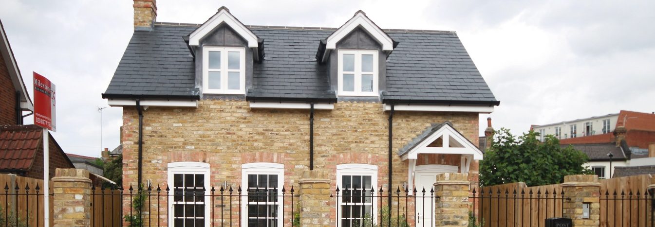 Two-storey, stone-built house with a slate roof and white windows, surrounded by a wooden fence.