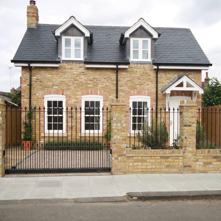 Stone cottage with a pitched roof, white windows, and a wooden fence in front.