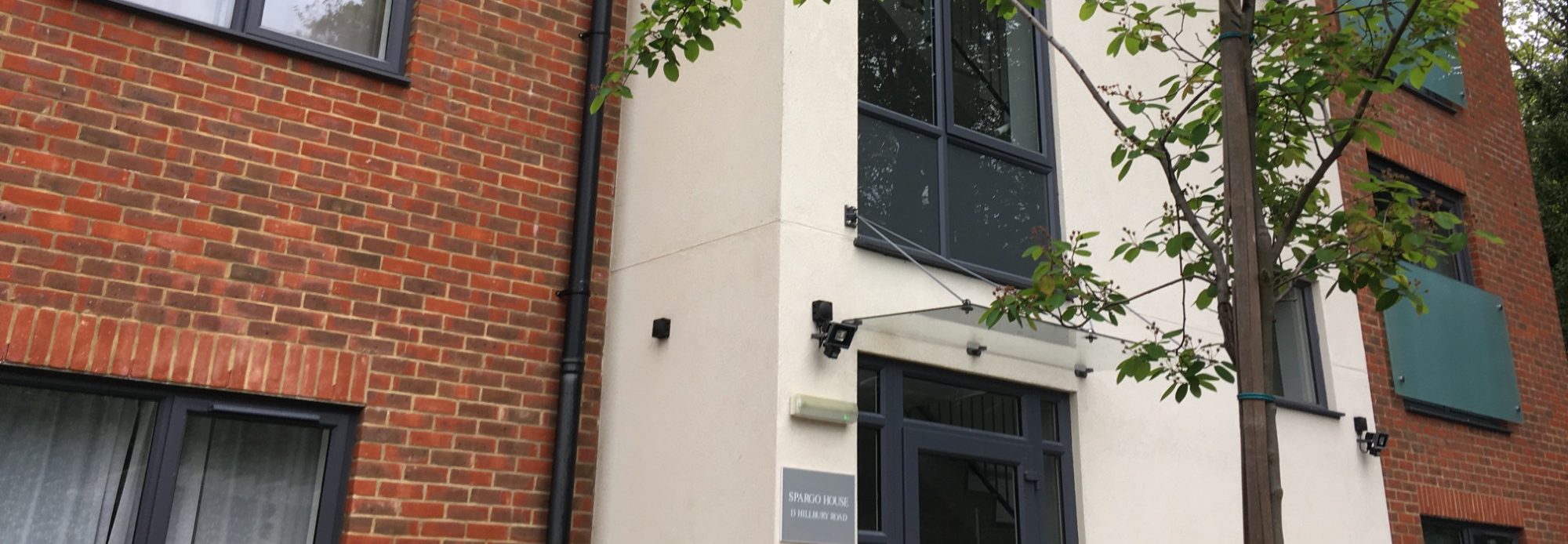 Modern building facade featuring red brick and light-coloured cladding with a black door.