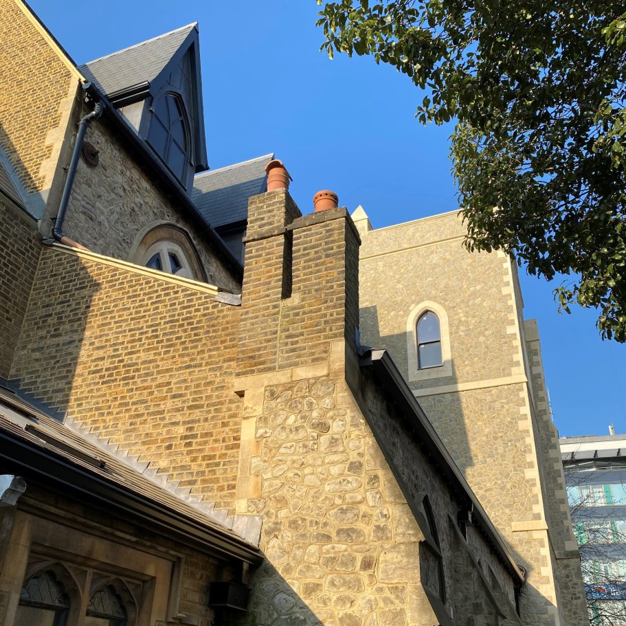 Stone building with chimney stacks under a clear blue sky and green foliage.