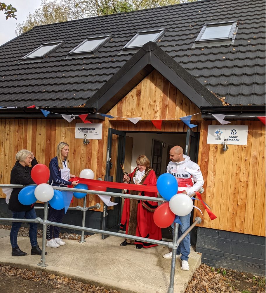 A group of people celebrating a ribbon-cutting ceremony outside a wooden building.