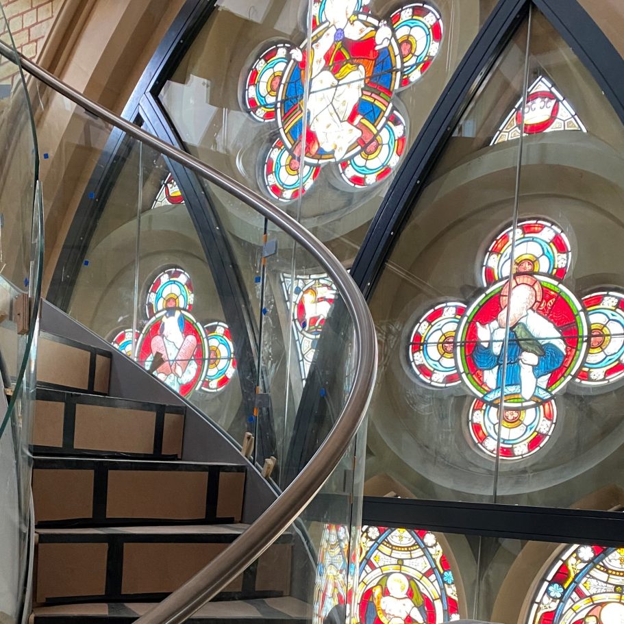 Curved staircase beside colourful stained glass windows in a church interior.