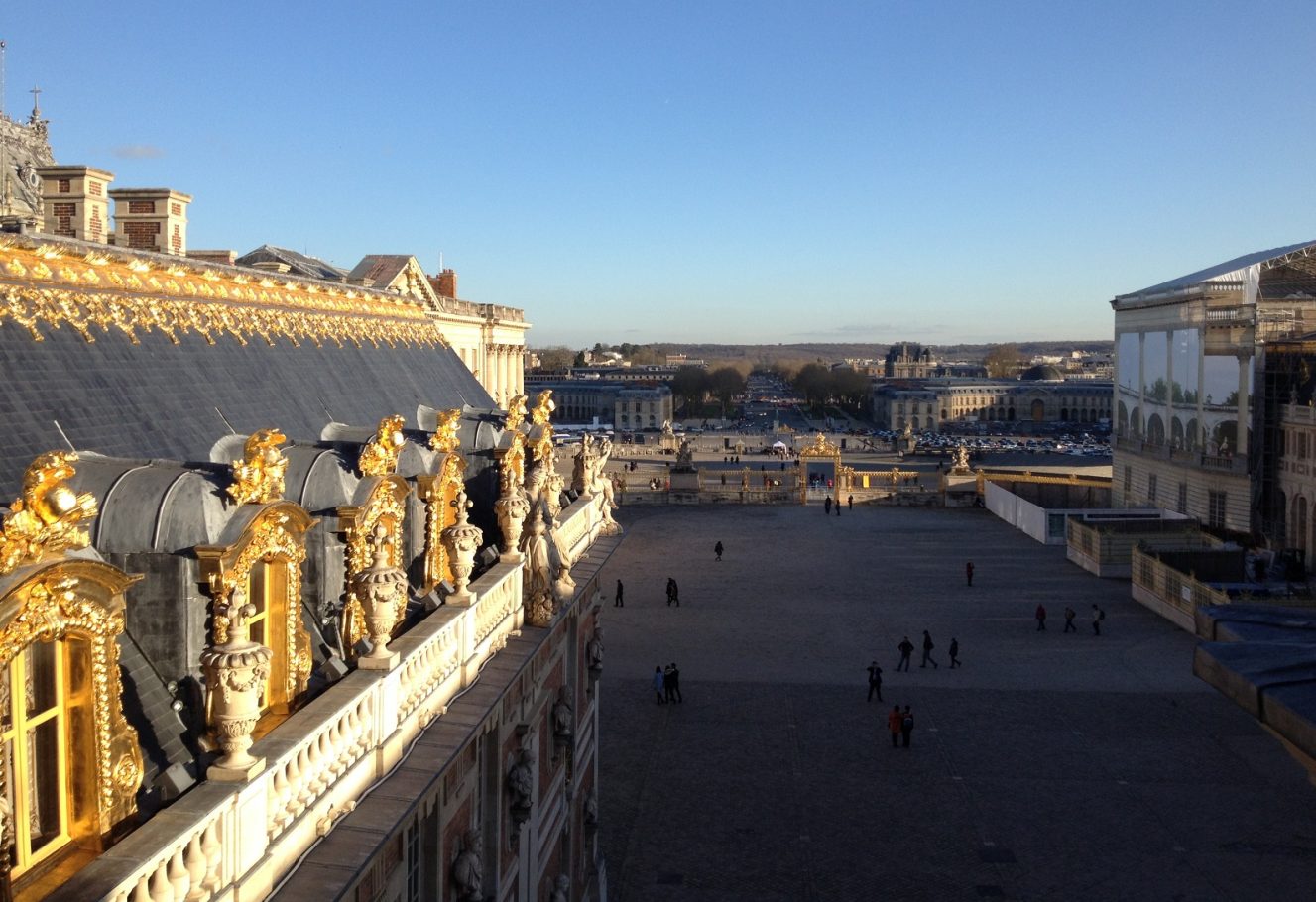View of the Palace of Versailles and its grounds under a clear blue sky.