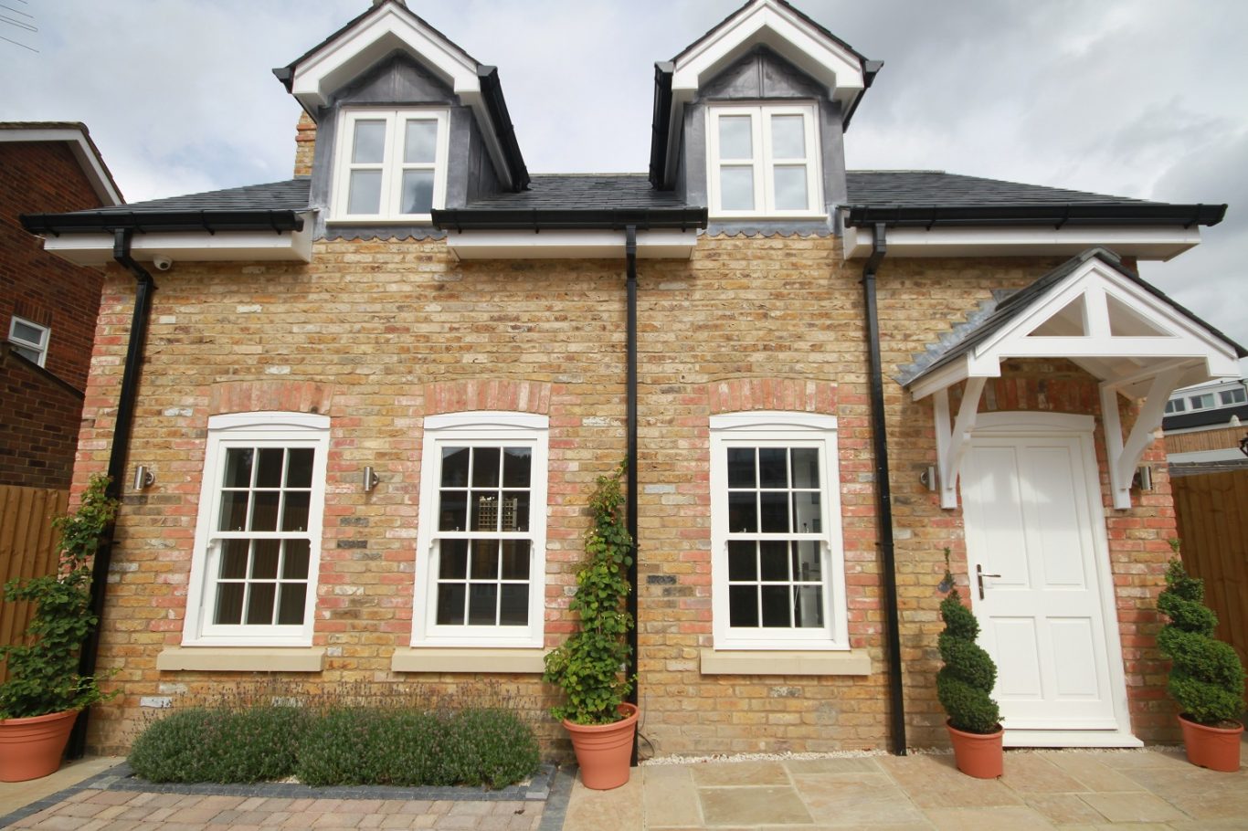 A brick house with white trim, two dormer windows, and potted plants at the entrance.