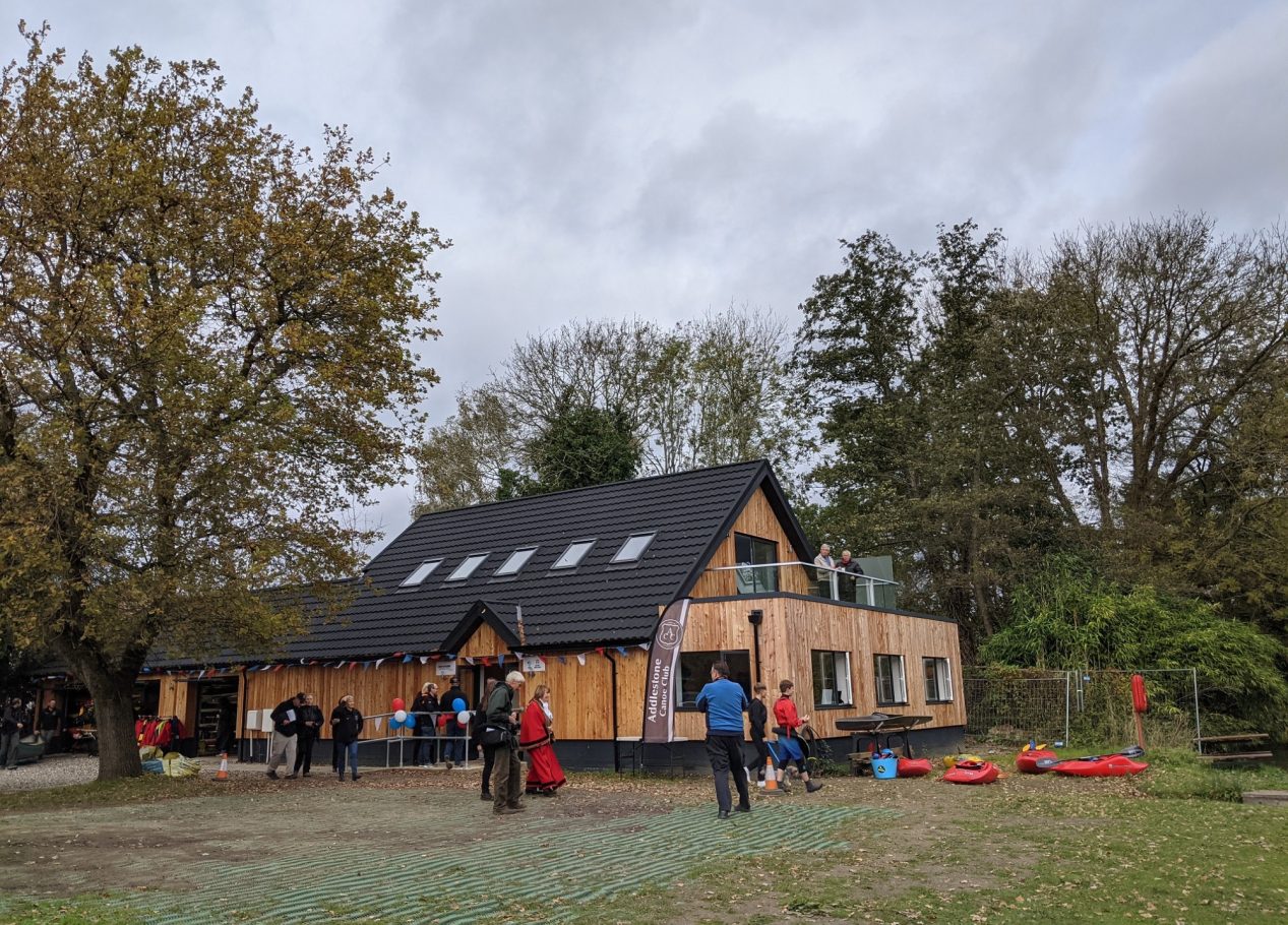 A modern wooden house with people gathering outside on a cloudy day.