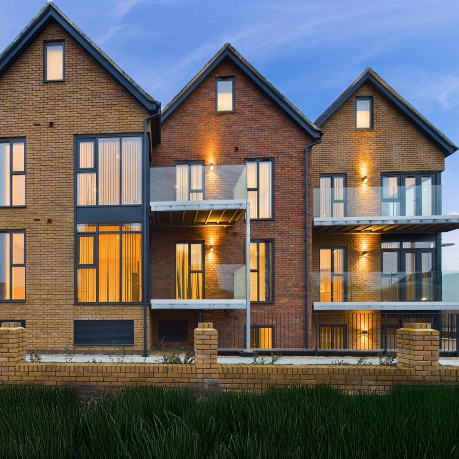 Modern brick townhouses with large windows and balconies, set against a twilight sky.