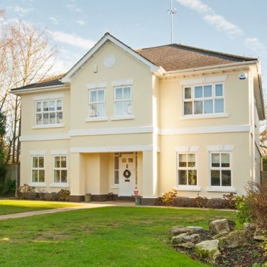 A two-storey yellow house with a front garden and well-maintained lawn.